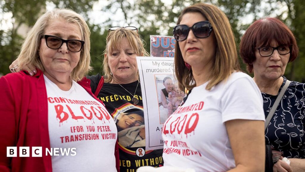 Four women who have been affected by the infected blood scandal attend a vigil in Parliament Square on 19 May, 2024 in London, England. Two of the women wear white t-shirts with "contaminated blood" printed on them in red ink.